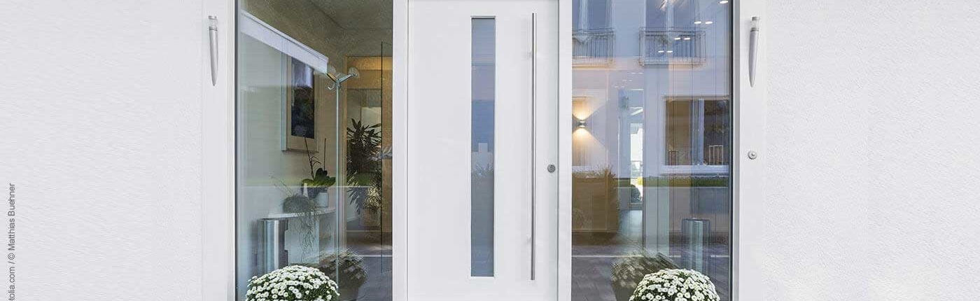 Weiße Eingangstür aus Aluminium eingefasst in vollformatige Glasscheiben rechts und links
