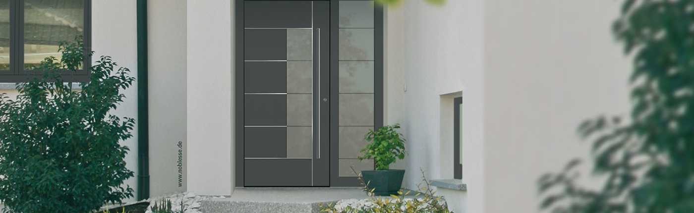 Ausschnitt Haus, Eingangstür aus Aluminium mit länglichem Glaseinsatz, rechts Glaseinsatz im Aluminiumrahmen