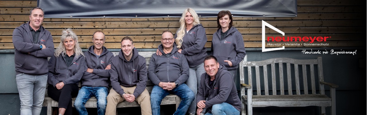 Das Team von Neumeyer sitzt auf einer Bank vor dem Firmengebäude